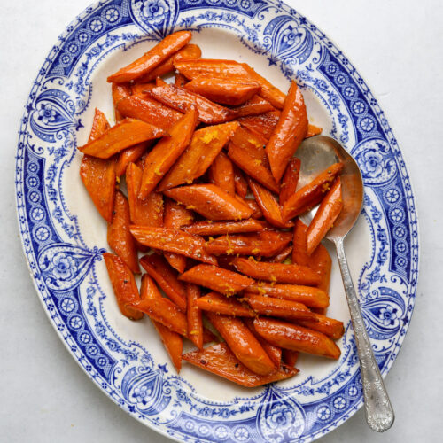 A blue and white antique platter filled with glossy roasted carrots with maple glaze.