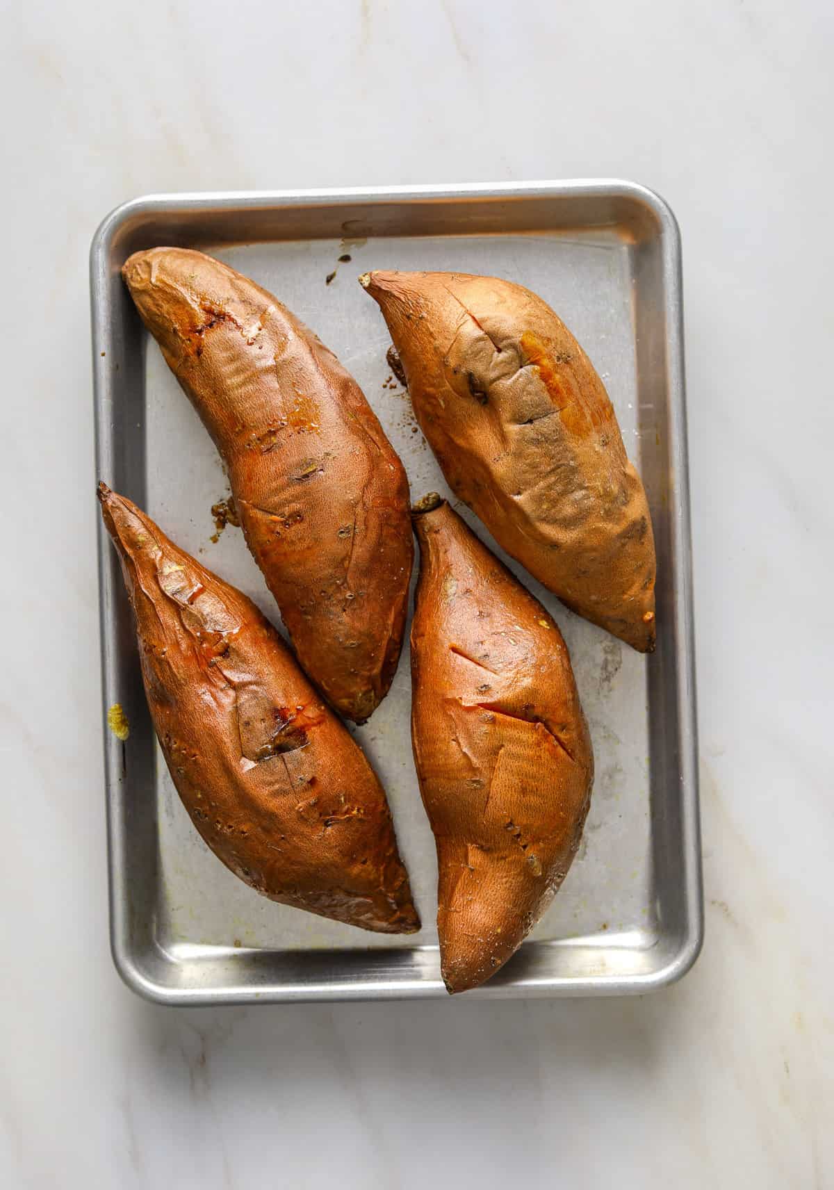 4 whole, roasted sweet potatoes on a baking tray.