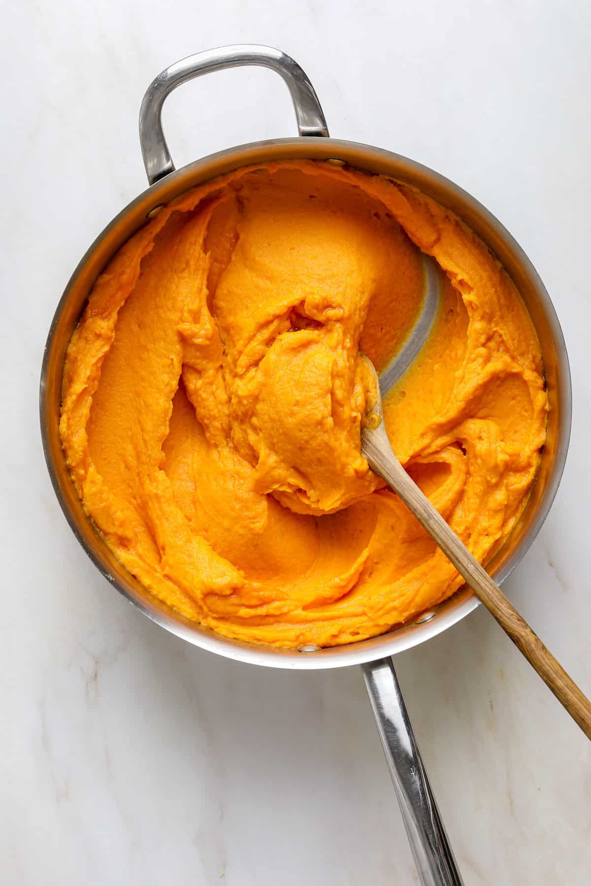 A large skillet filled with puréed sweet potatoes and a wooden spoon.