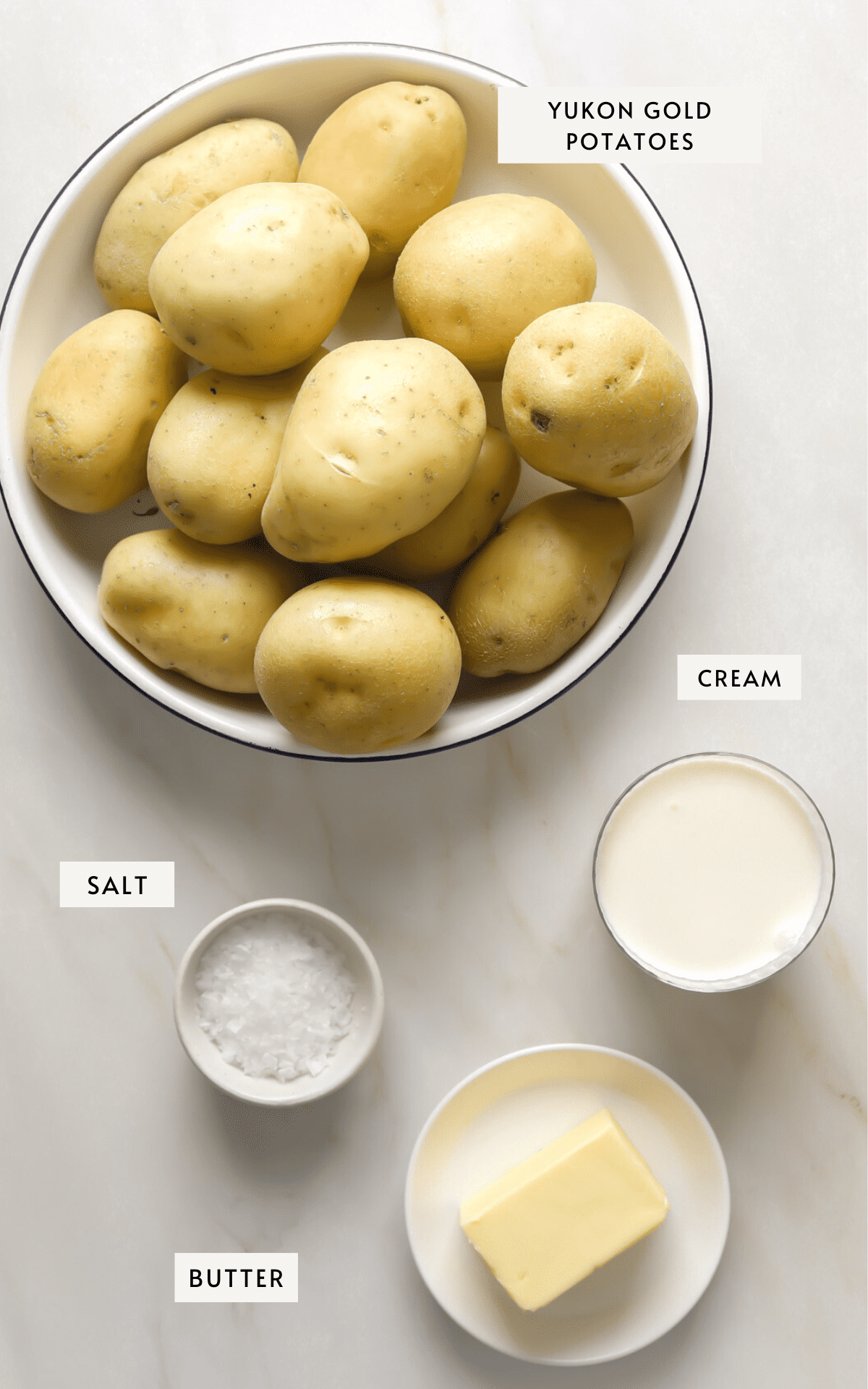 A bowl of Yukon gold potatoes, small dishes of cream, butter and salt.