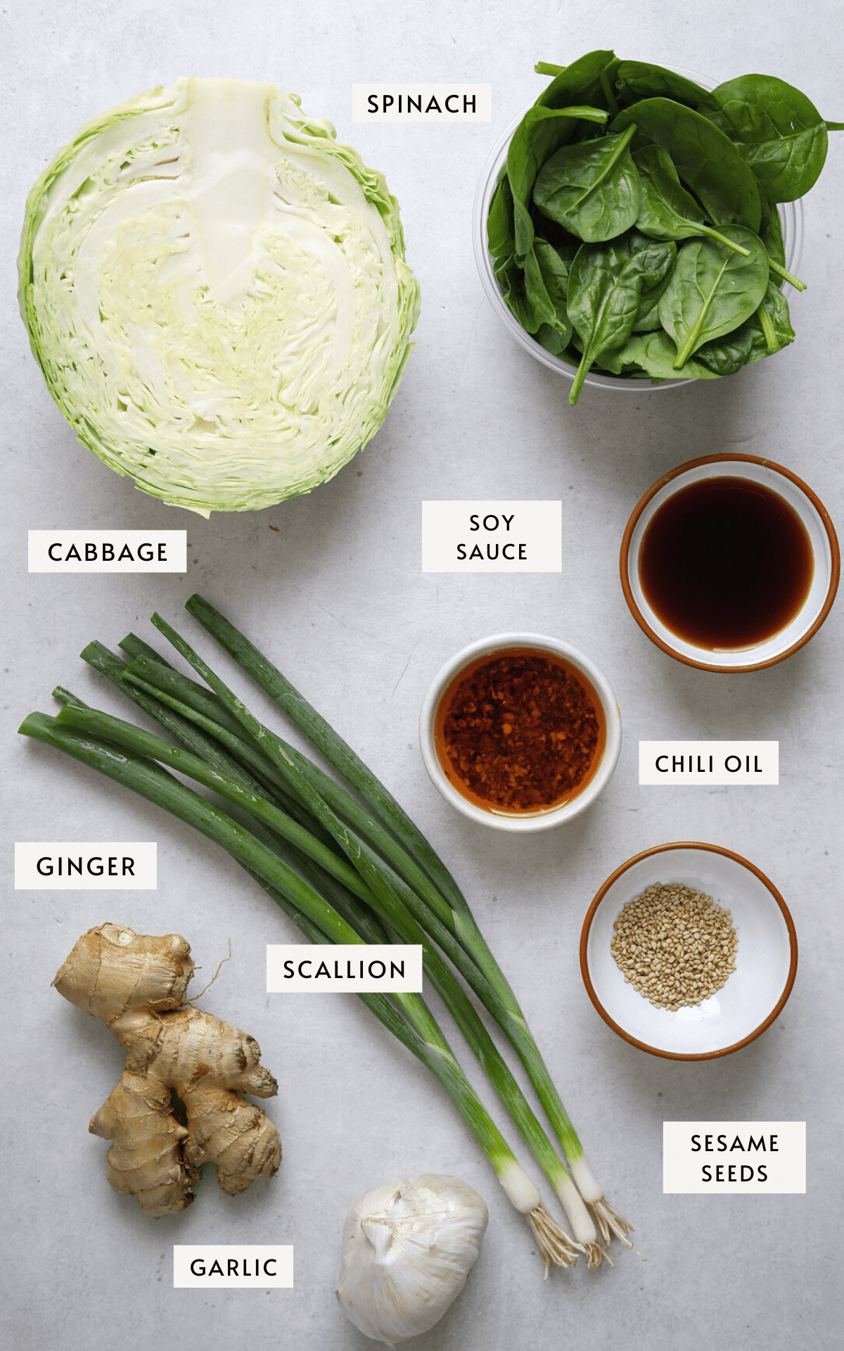 One whole head of cabbage cut in half, a cup of baby spinach, tiny dishes of; chili oil, sesame seeds and soy sauce, a whole head of garlic and a large knob of ginger.