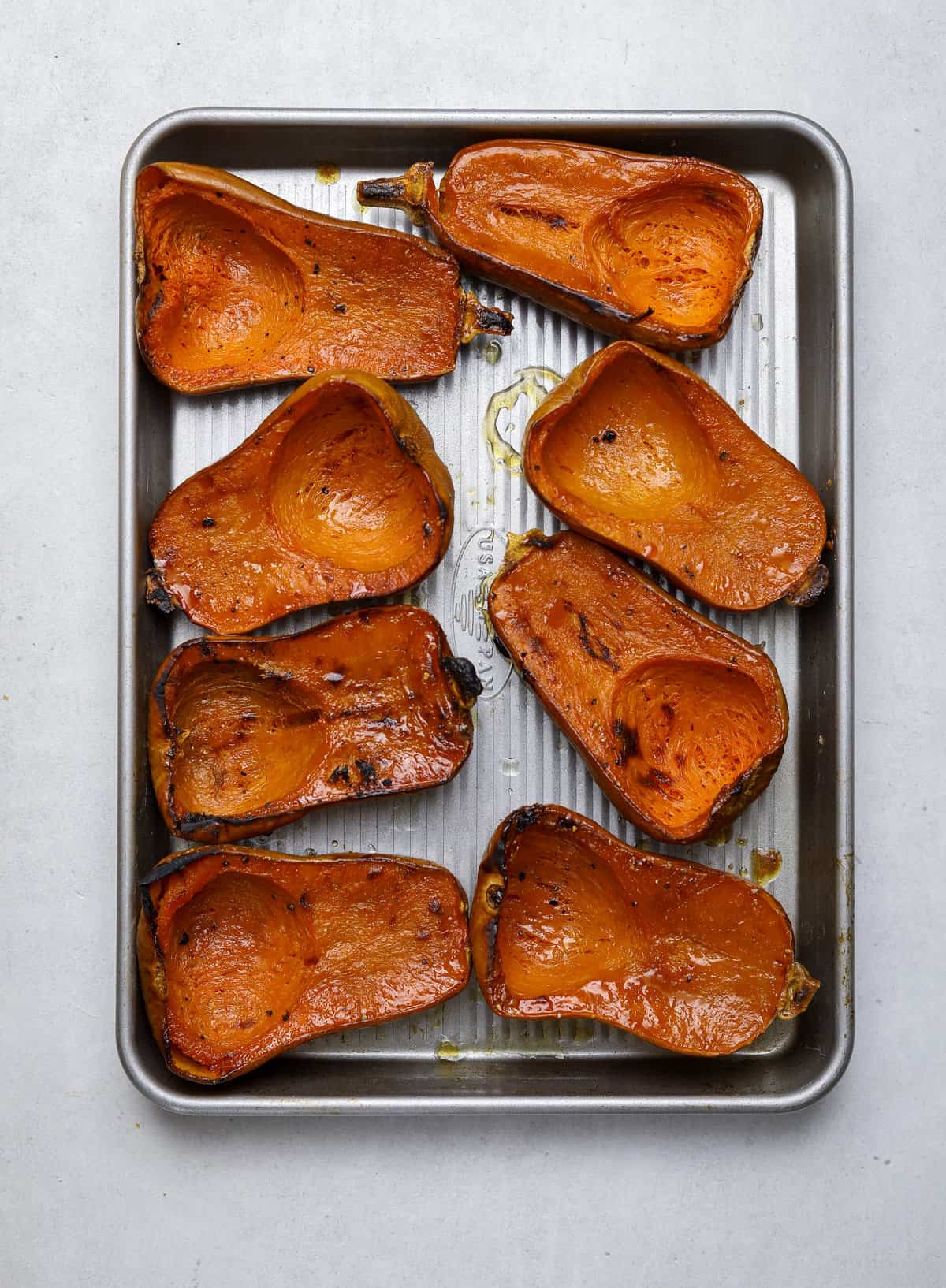 a baking tray filled with halved, roasted squash.