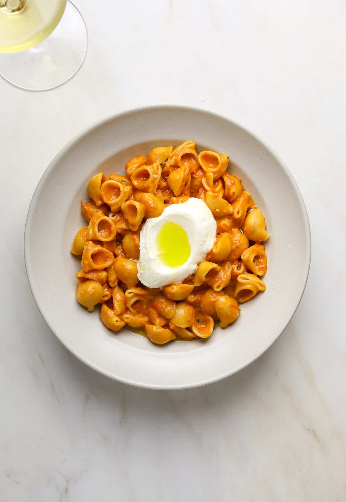 A white bowl filled with saucy red pasta topped with a dollop of ricotta cheese.