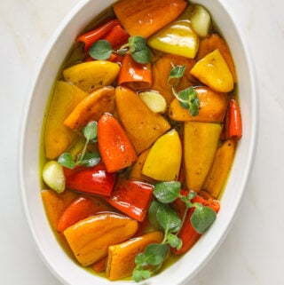 A white oval bowl filled with multi-colored roasted red peppers, oregano and garlic.