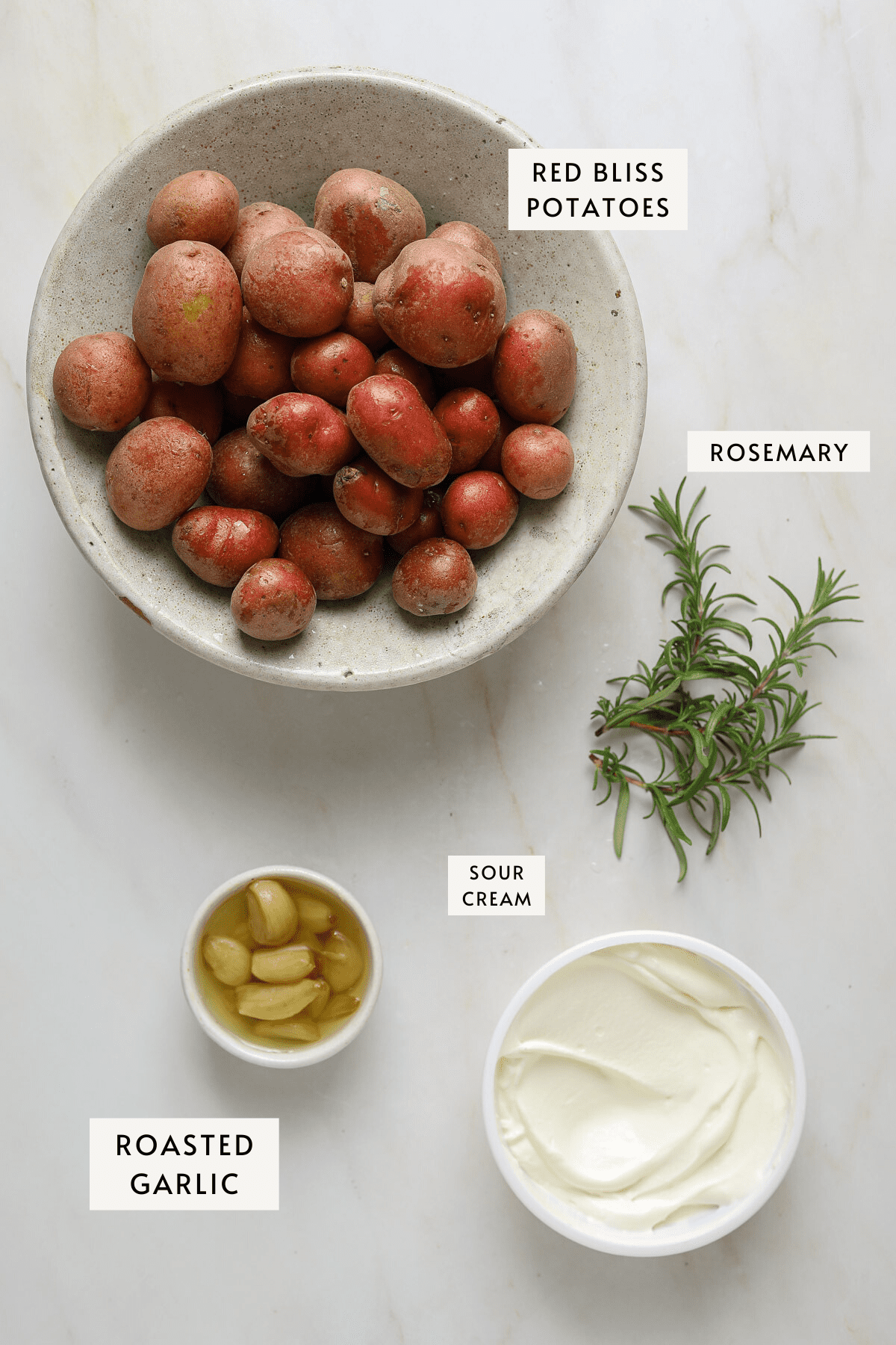 A bowl or red bliss potatoes, three sprigs of rosemary, a small bowl of roasted garlic cloves, a tub of sour cream.