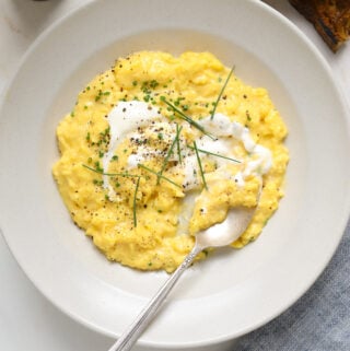 A white bowl filled with scrambled eggs, chopped chives and a silver spoon.
