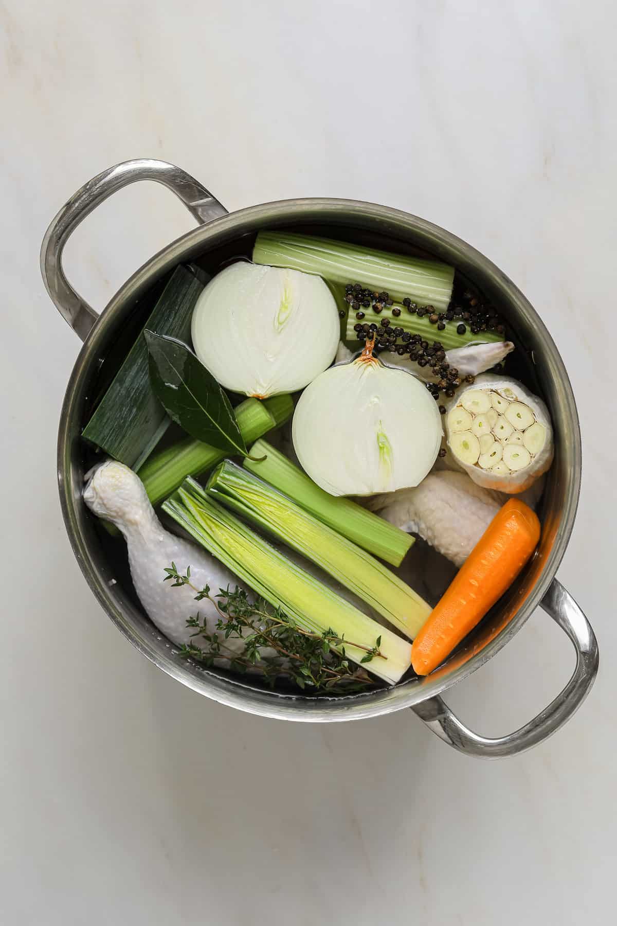 A pot of water full of raw chicken bones, leeks, garlic, peppercorns and celery.