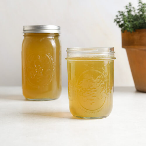 One large jar and one small jar of chicken stock on a white background.