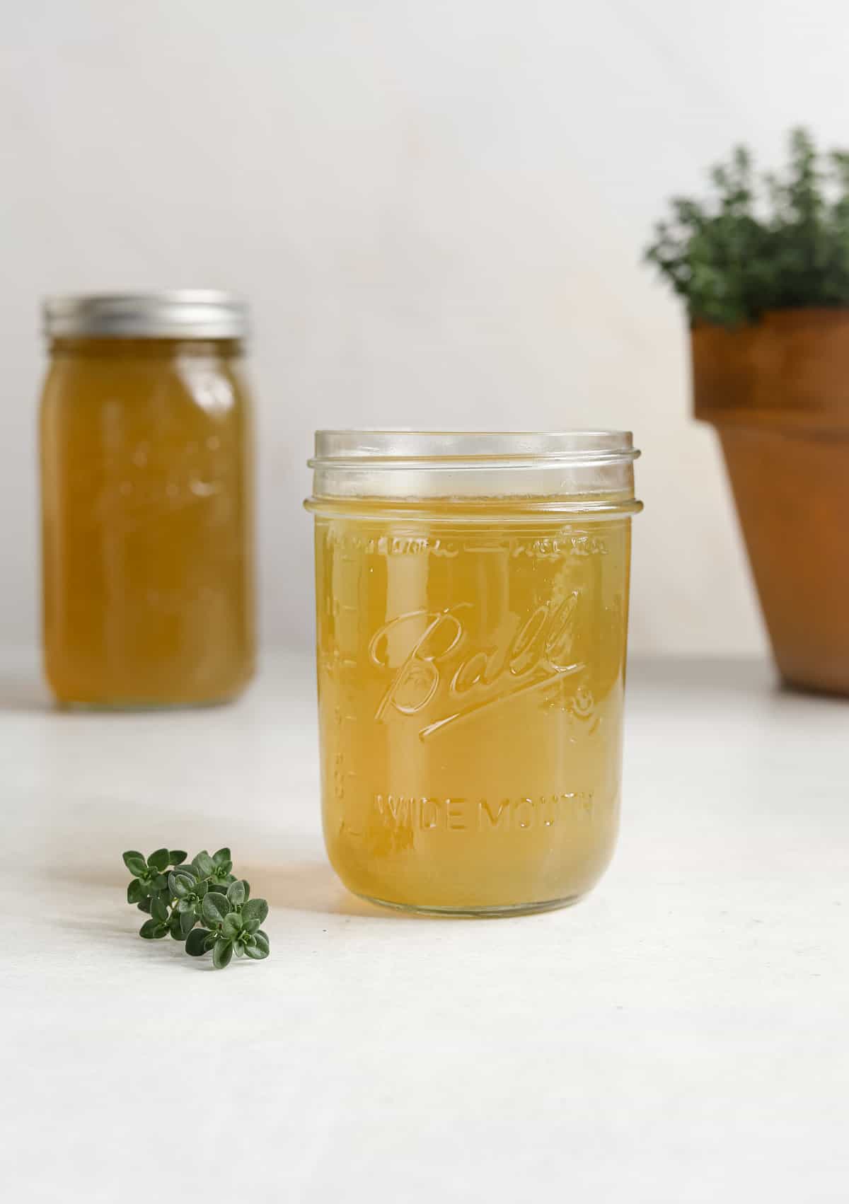A mason jar filled with chicken stock next to a small sprig of fresh thyme.