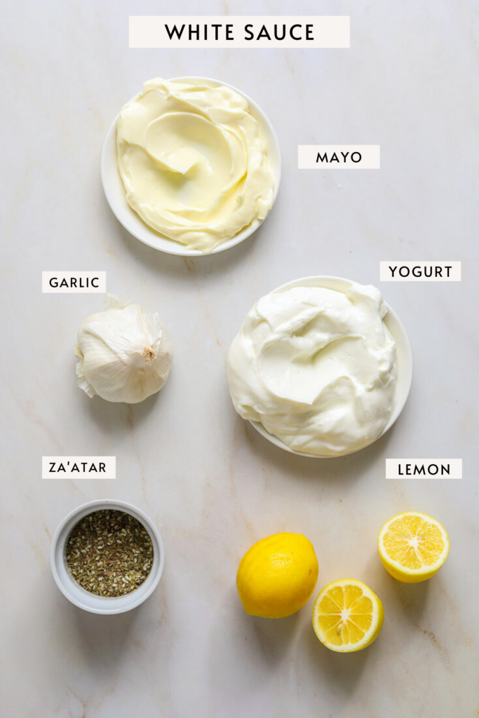 Small bowls of yogurt, mayo, a bulb of garlic, lemons and za'atar spice.