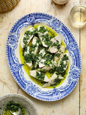 A blue and white antique platter filled with slices of chicken topped with a fresh green herb sauce on a wooden table top.