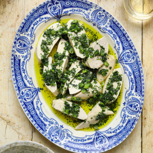 A blue and white antique platter filled with slices of chicken topped with a fresh green herb sauce on a wooden table top.