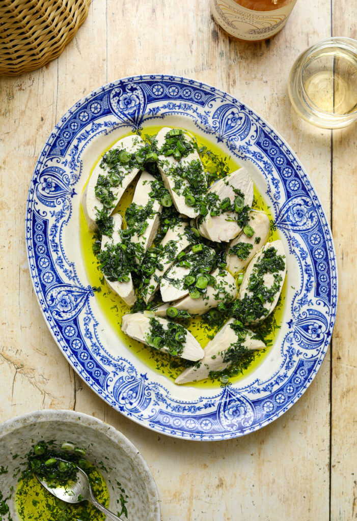 A blue and white antique platter filled with slices of chicken topped with a fresh green herb sauce on a wooden table top.