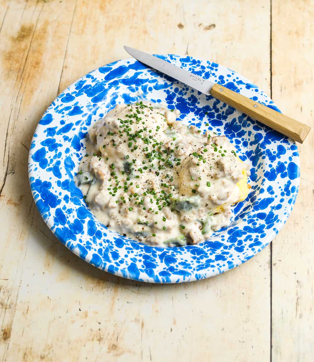A blue and white enamel plate filled with biscuits and gravy topped with black pepper and minced chives.