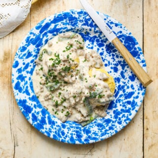 A blue and white enamel plate with yellow corn biscuits and gravy speckled with roasted poblano peppers on a wooden table top.