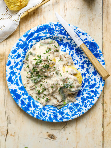 A blue and white enamel plate with yellow corn biscuits and gravy speckled with roasted poblano peppers on a wooden table top.