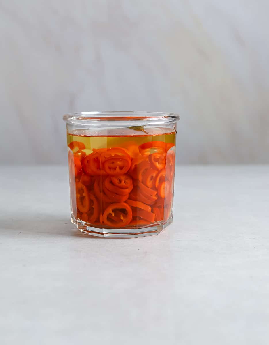 A small glass jar filled with red pickled chilis.