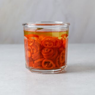 A small glass jar filled with red pickled chilis.