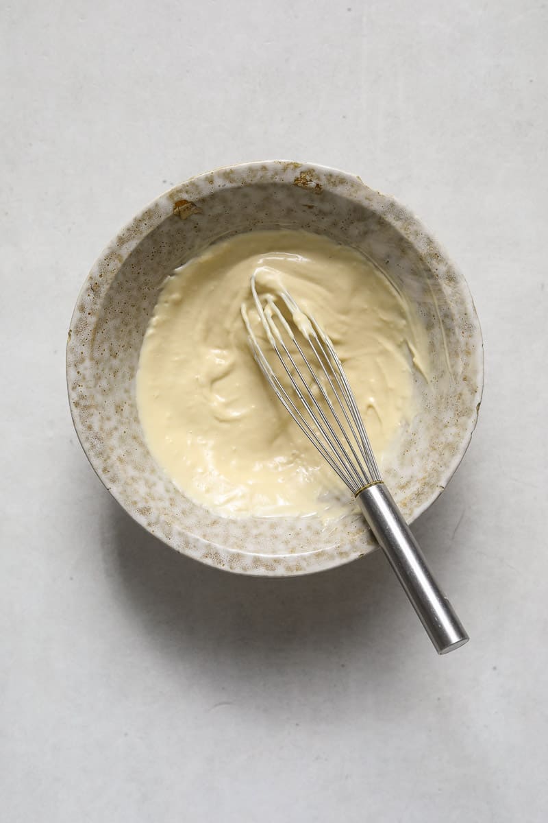 A small ceramic bowl filled with creamy mayo sauce and a small whisk.