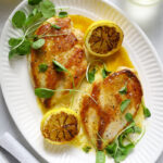 Two golden, seared chicken breasts on a white platter, drizzled with lemon vinaigrette.