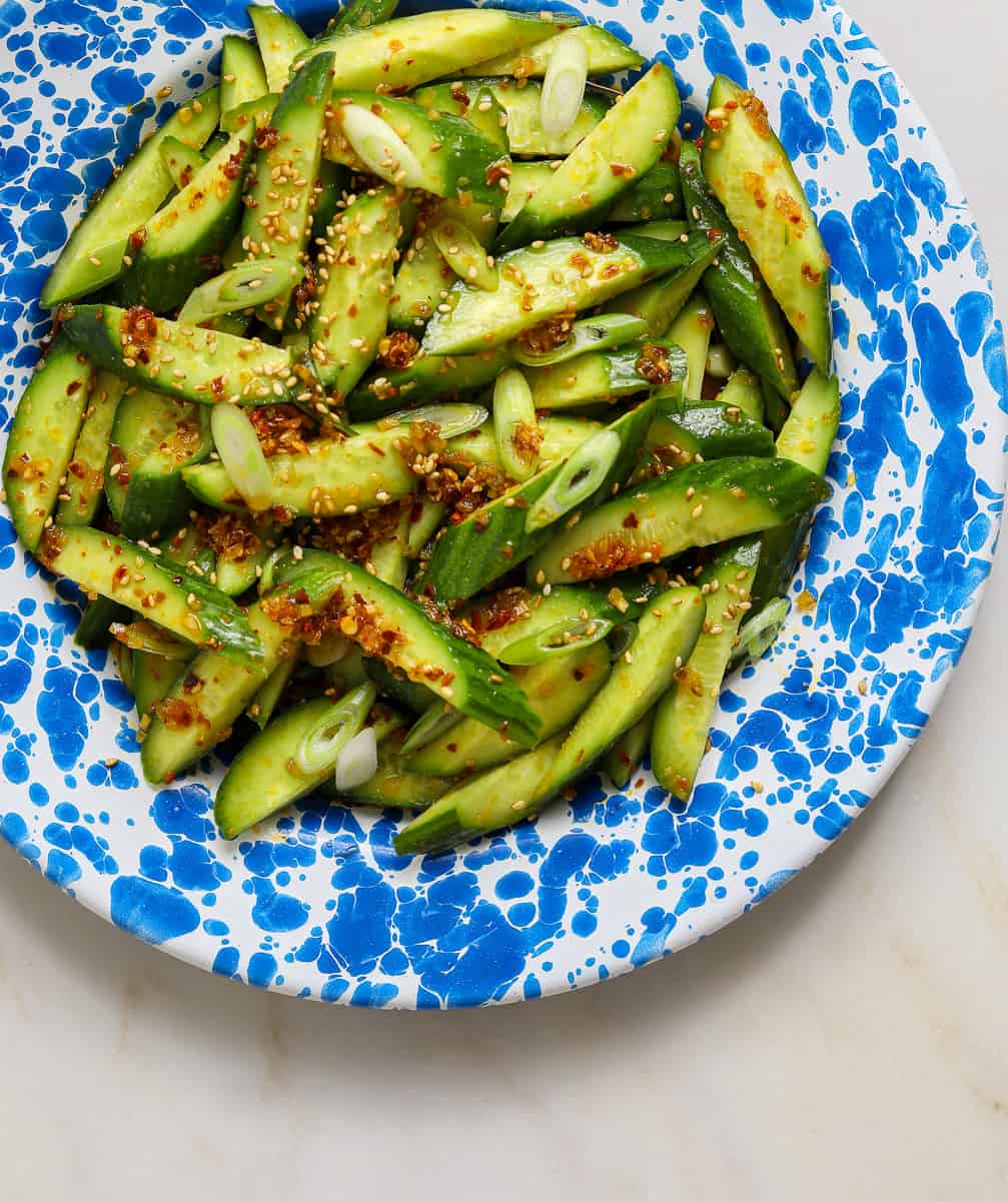 A blue and white enamel plate filled with spicy cucumber and thinly sliced scallions.