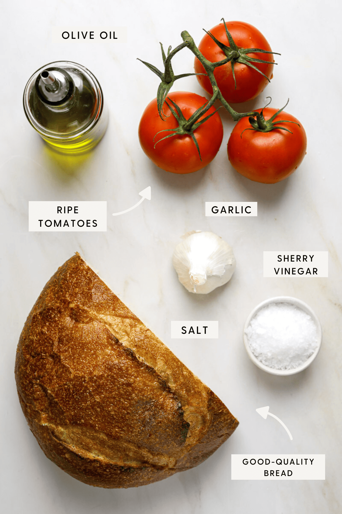 Half a loaf of bread, a bunch of three ripe tomatoes on the vine, a bottle of olive oil, a bulb of garlic and a bowl of flakey sea salt.