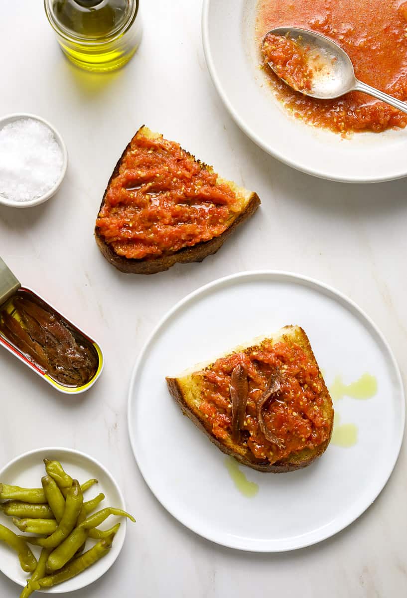 Two halves of toasted bread topped with tomato puree, olive oil and spanish anchovy.
