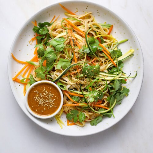 A white ceramic bowl filled with a vibrant rice noodle and vegetable salad.
