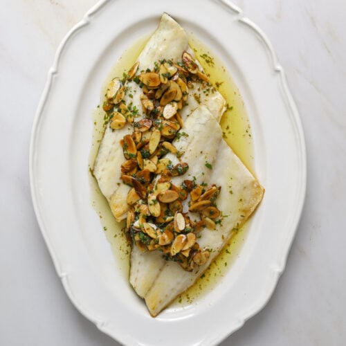 A white, oval platter with two fish filets and almond sauce.