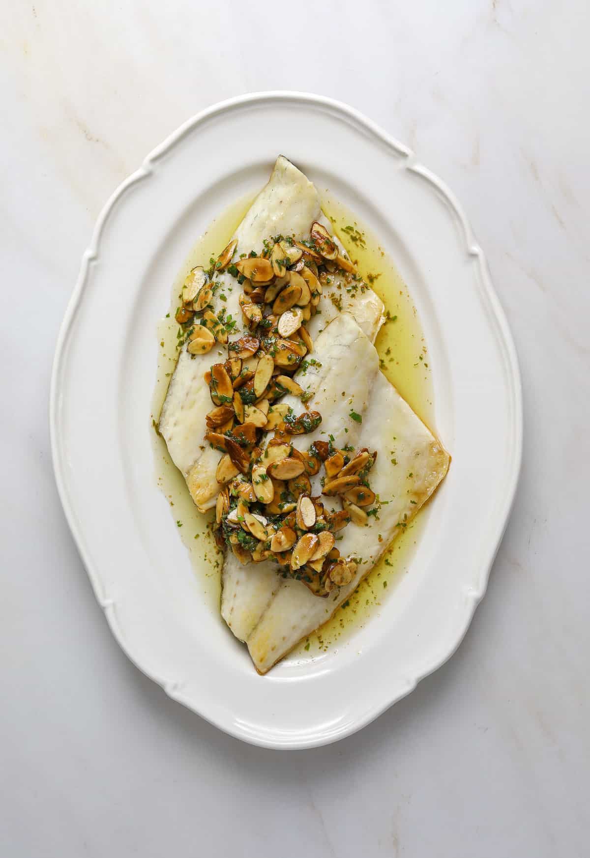 A white, oval platter with two fish filets and almond sauce.