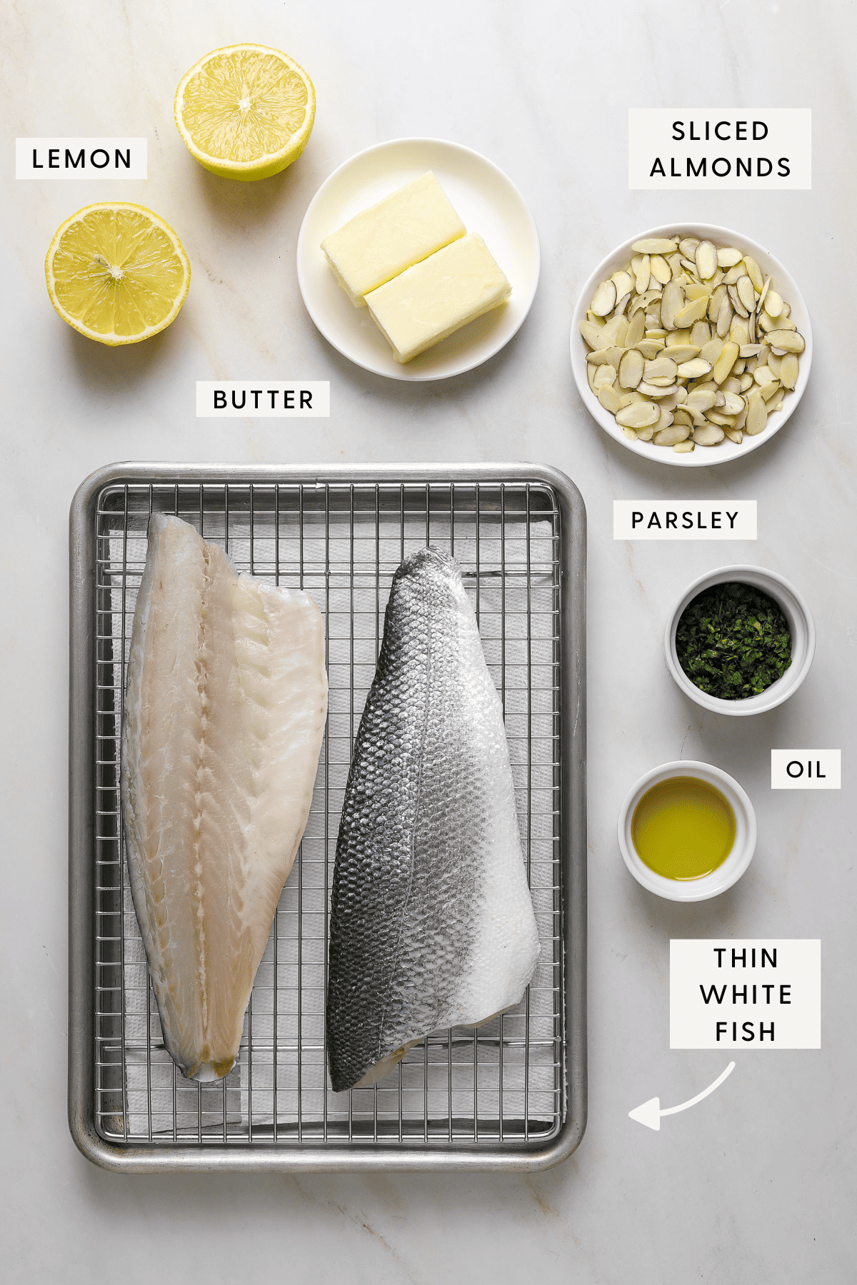 Fish on a baking tray, small dishes of recipe ingredients; chopped parsley, sliced almonds, butter, oil and lemons.