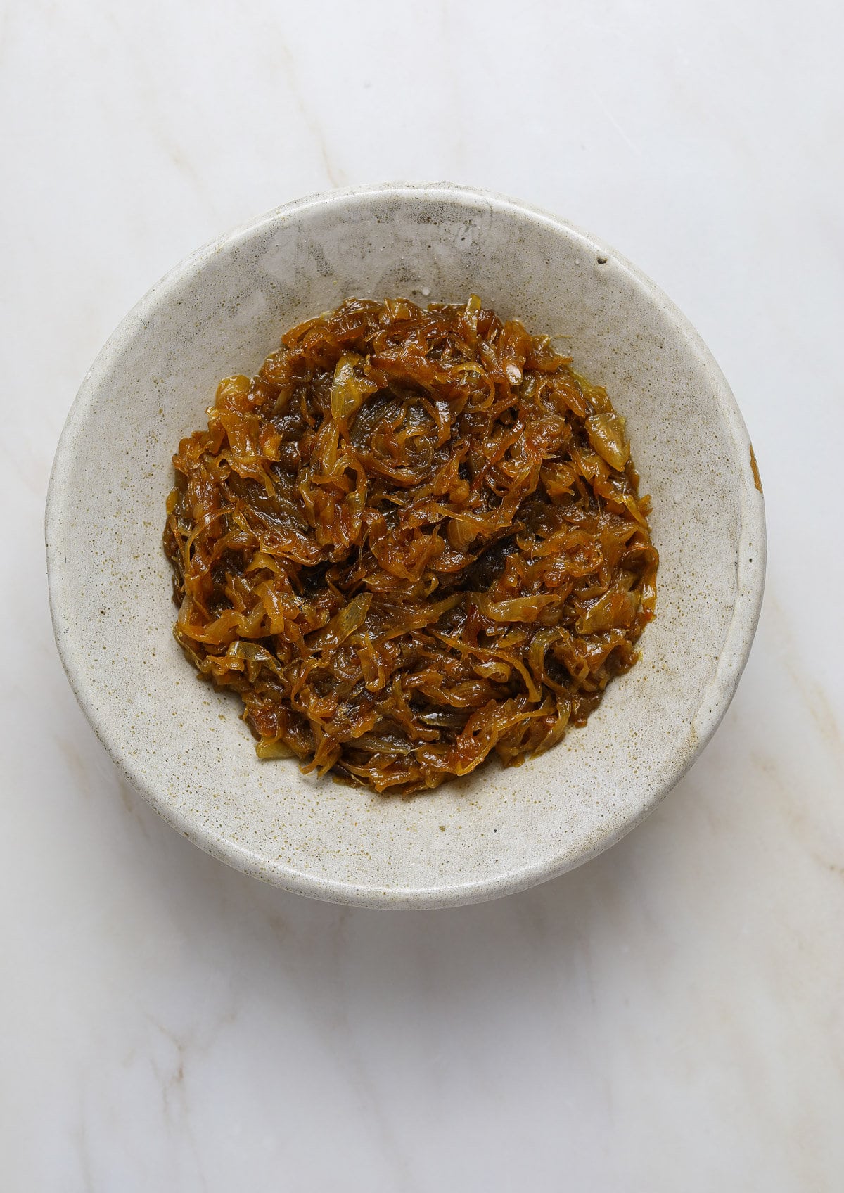 A ceramic bowl of caramelized onions on a marble background.
