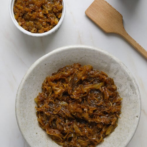 A large bowl of dark brown, caramelized onions with wooden spatula and a bottle of olive oil