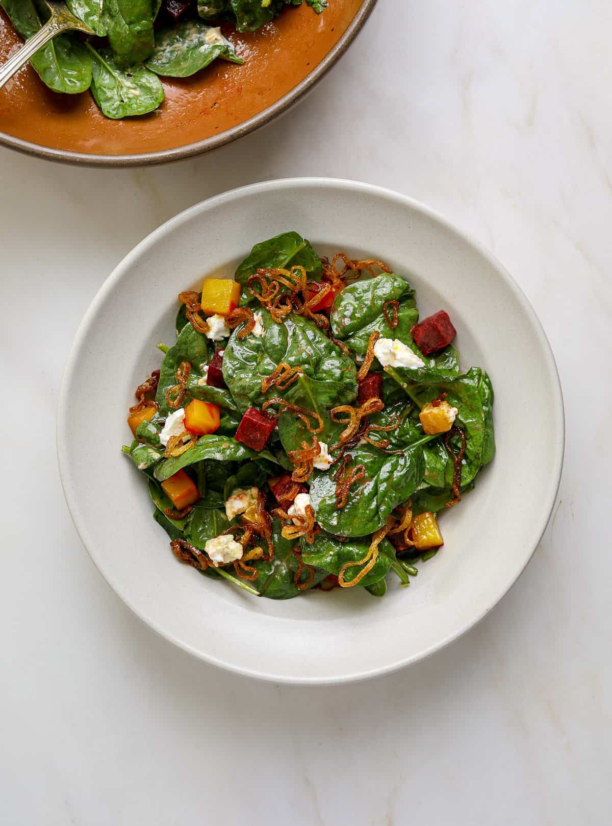 A white bowl filled with spinach salad, beets and goat cheese.