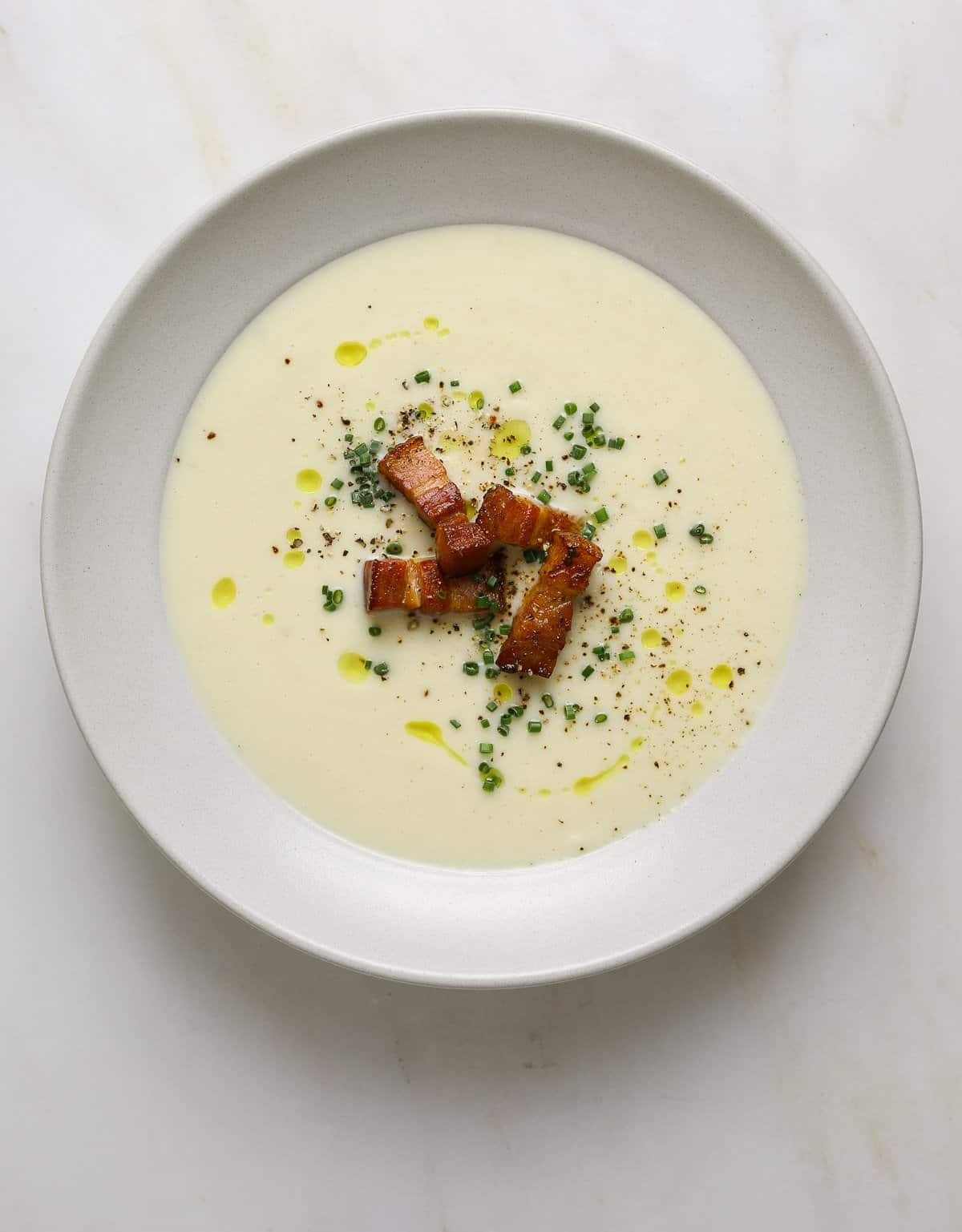 A bowl of white soup topped with minced chives, bacon and olive oil.