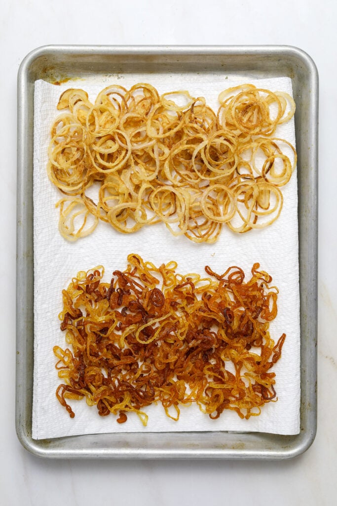 A paper towel lined baking tray with two different types of fried shallots.