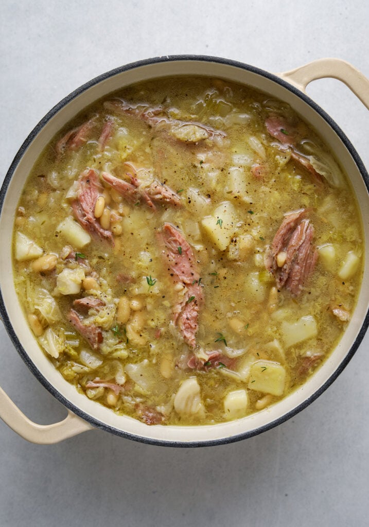 A pot of stew with potatoes, ham and beans.