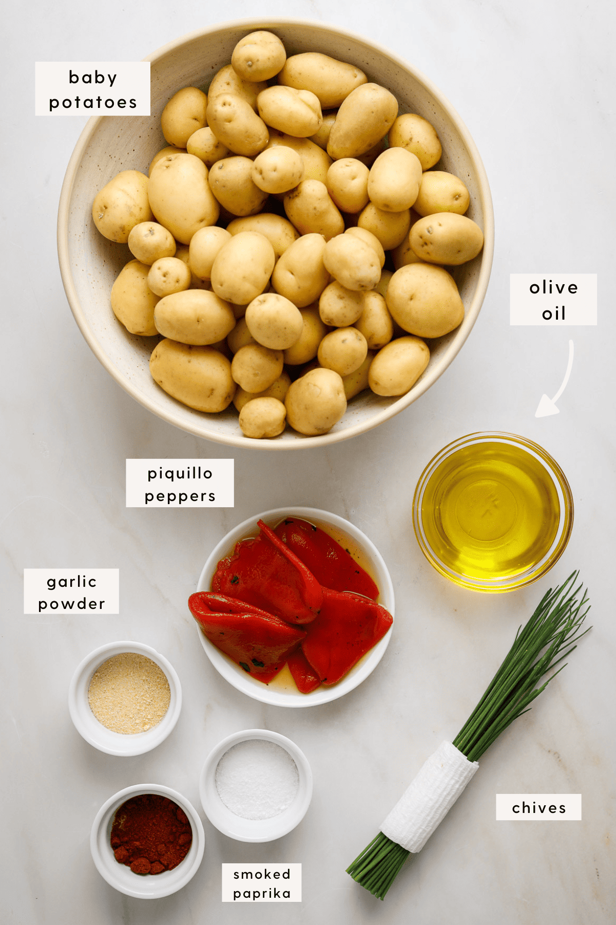 Recipes ingredients portioned into small bowls; olive oil, seasonings, chives, roasted peppers and small gold potatoes.