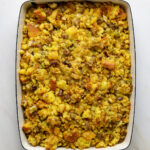 A large, blue enamel baking tray filled with cornbread stuffing on a marble tabletop.
