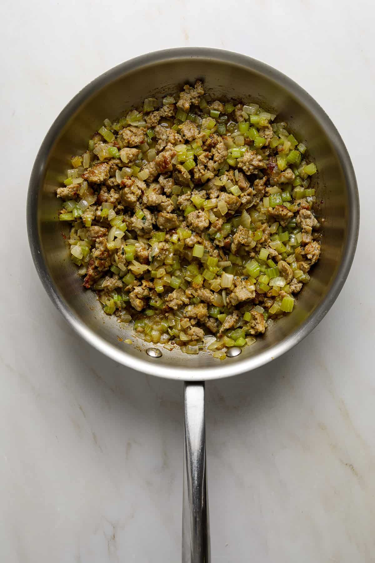 A stainless steel sauté pan filled with sausage, celery and onions.