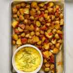A baking tray filled with roasted potatoes, a small dish of scrambled eggs and a large serving spoon.