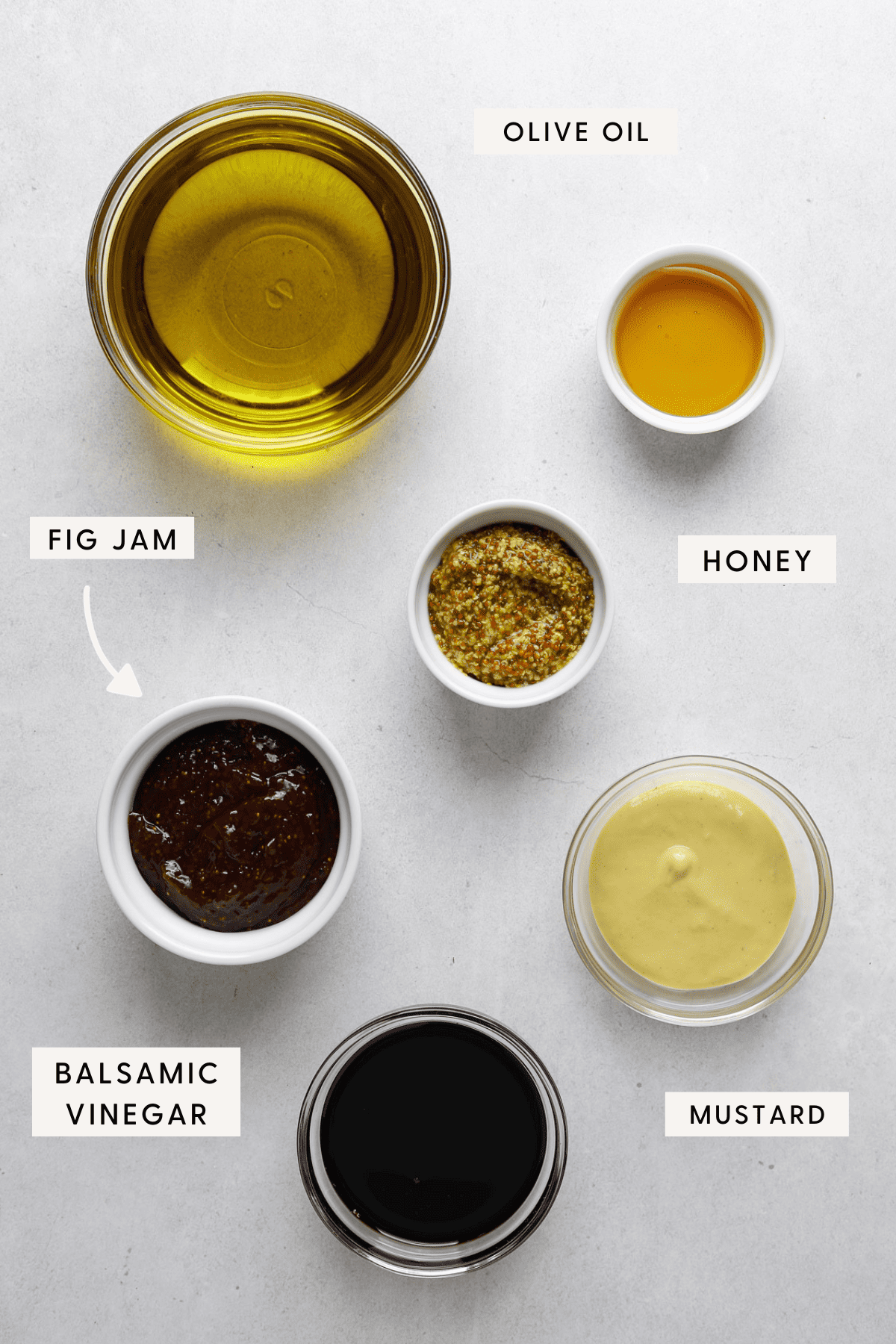 Individual bowls of salad dressing ingredients on a gray concrete tabletop.