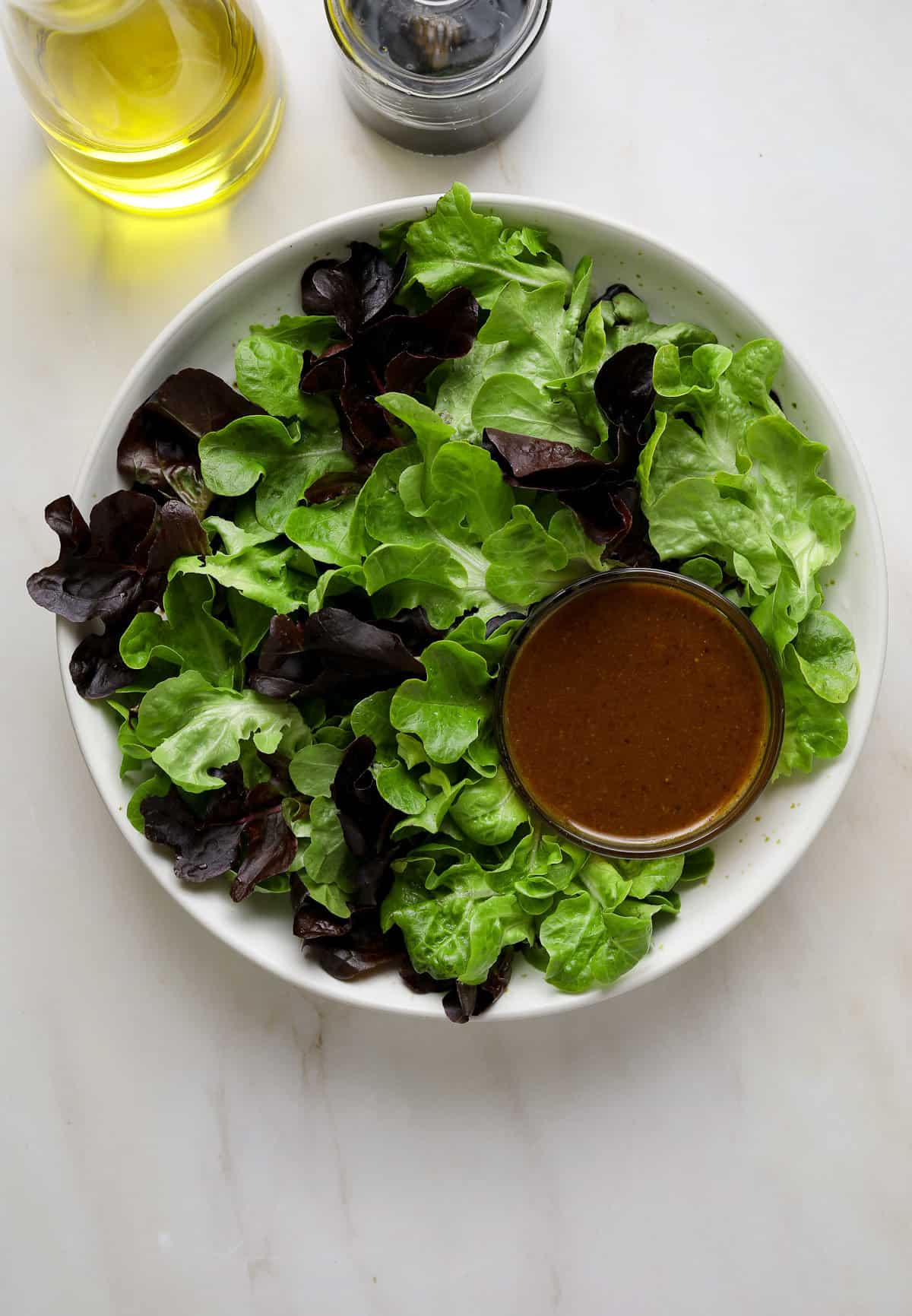 A bowl of bright green and purple lettuces with a small dish of vinaigrette salad dressing.