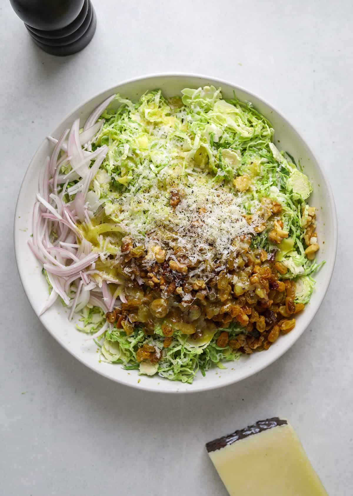 A bed of thinly sliced brussels sprouts topped with golden raisins, sliced shallots and cheese.