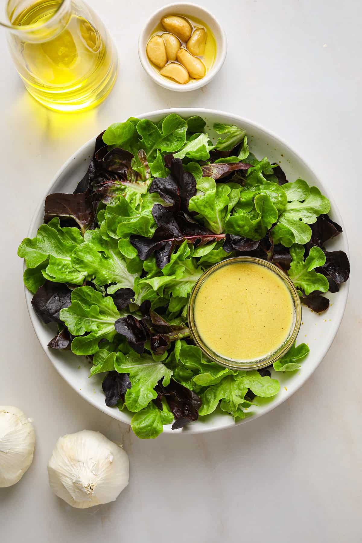 A bowl of lettuce with a small dish of creamy pale yellow salad dressing.