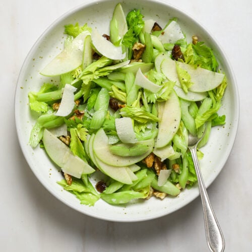 A white bowl of celery salad with a silver spoon.