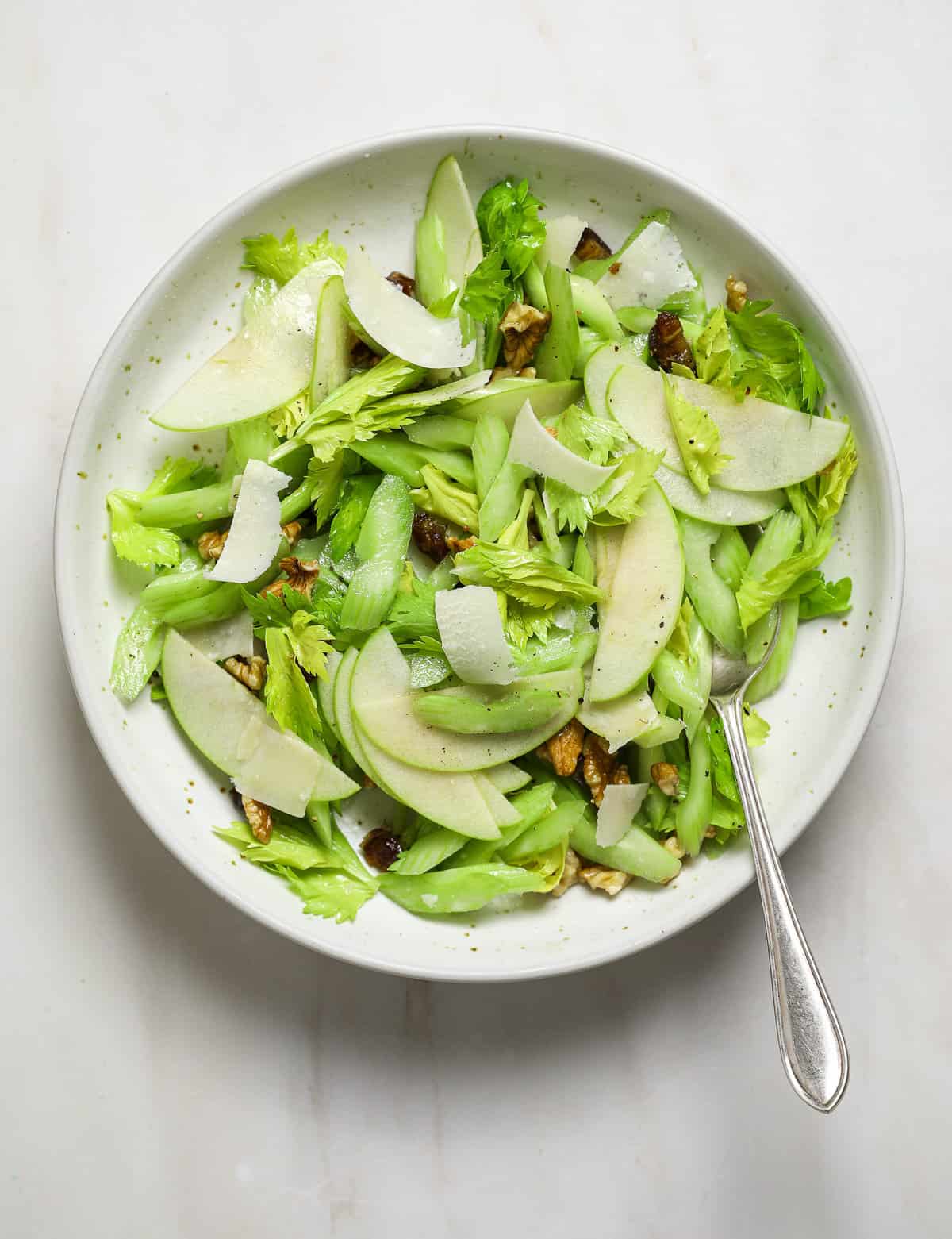 A white bowl of celery salad with a silver spoon.