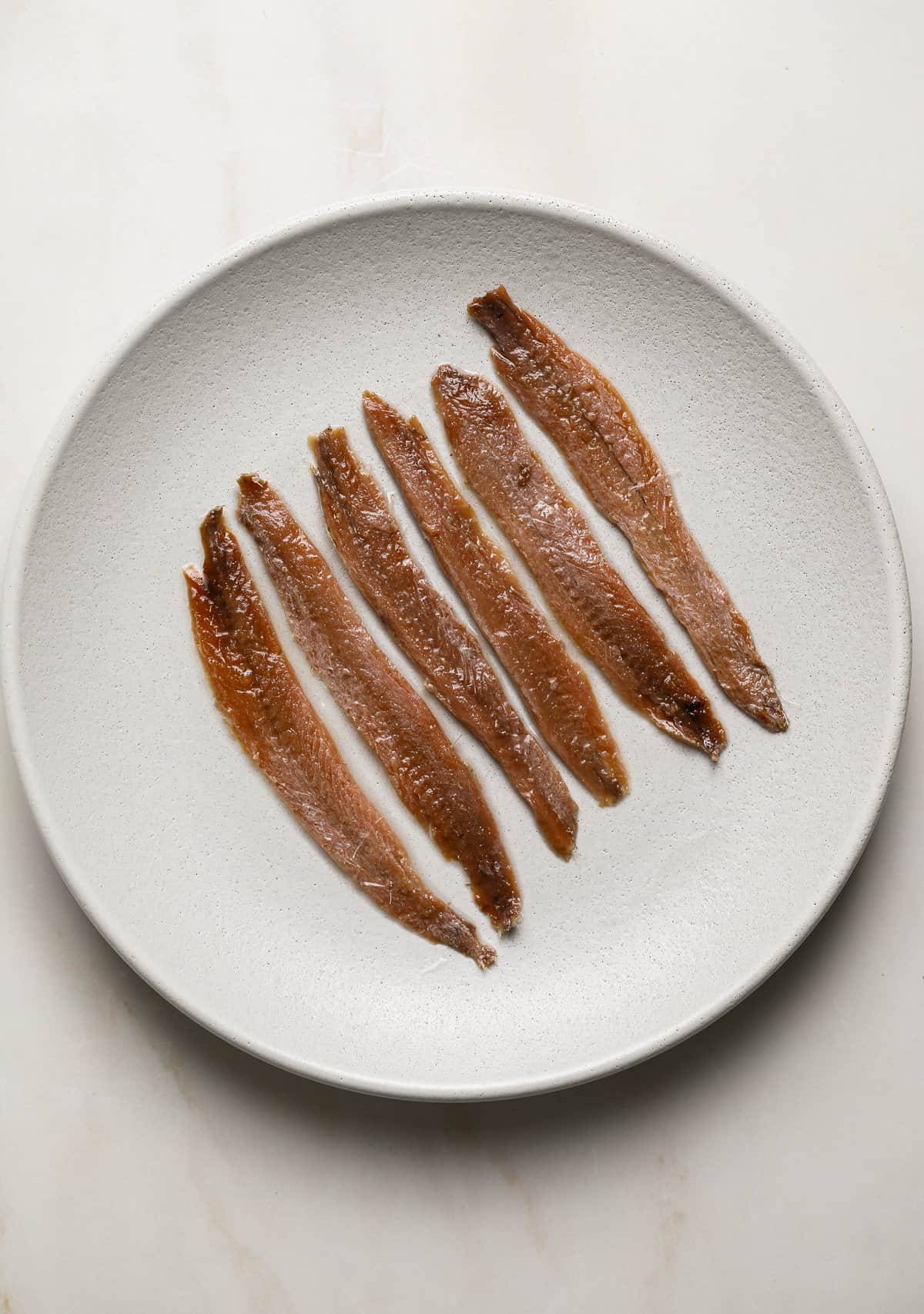 A plate of filled with 6 brown anchovies.
