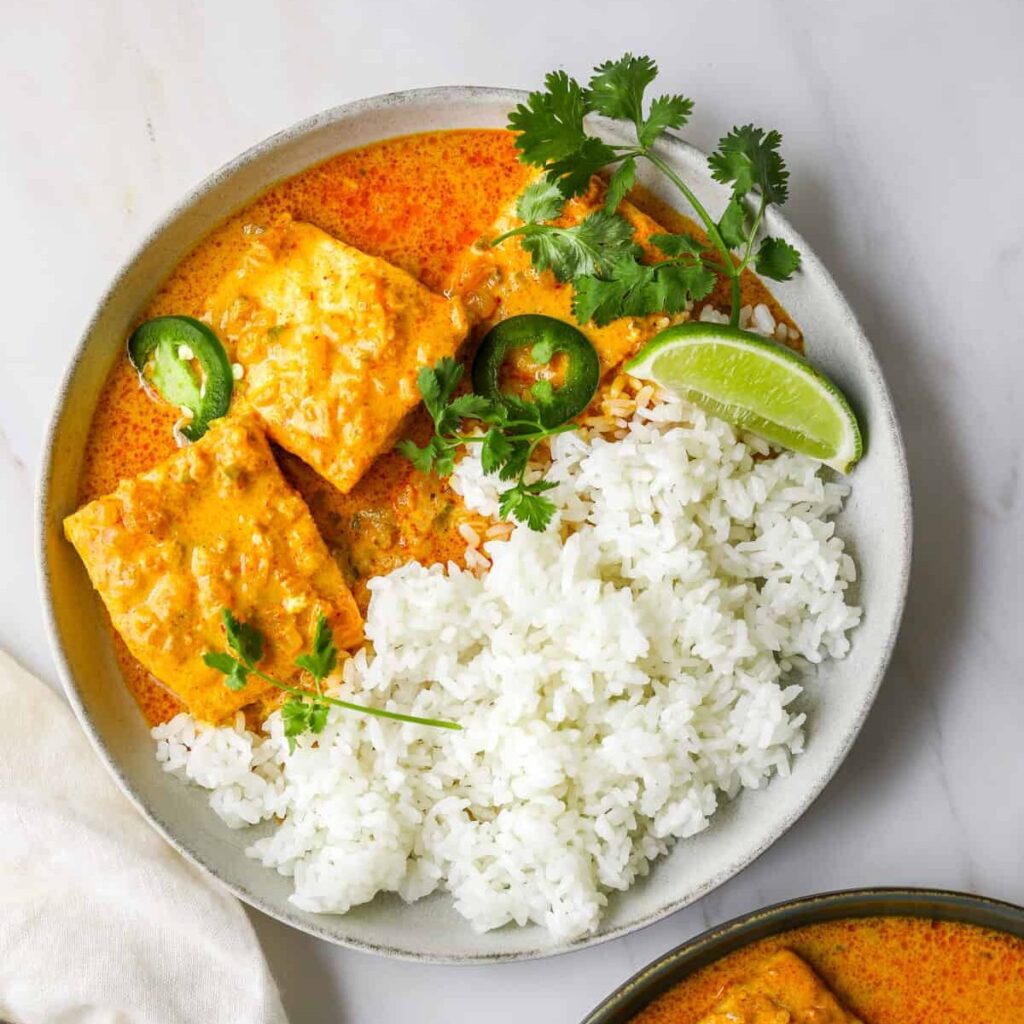 a white bowl filled with coconut curry braised salmon with limes, rice and cilantro