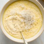 A white speckled ceramic bowl filled with cooked polenta and topped with grated parmesan cheese.